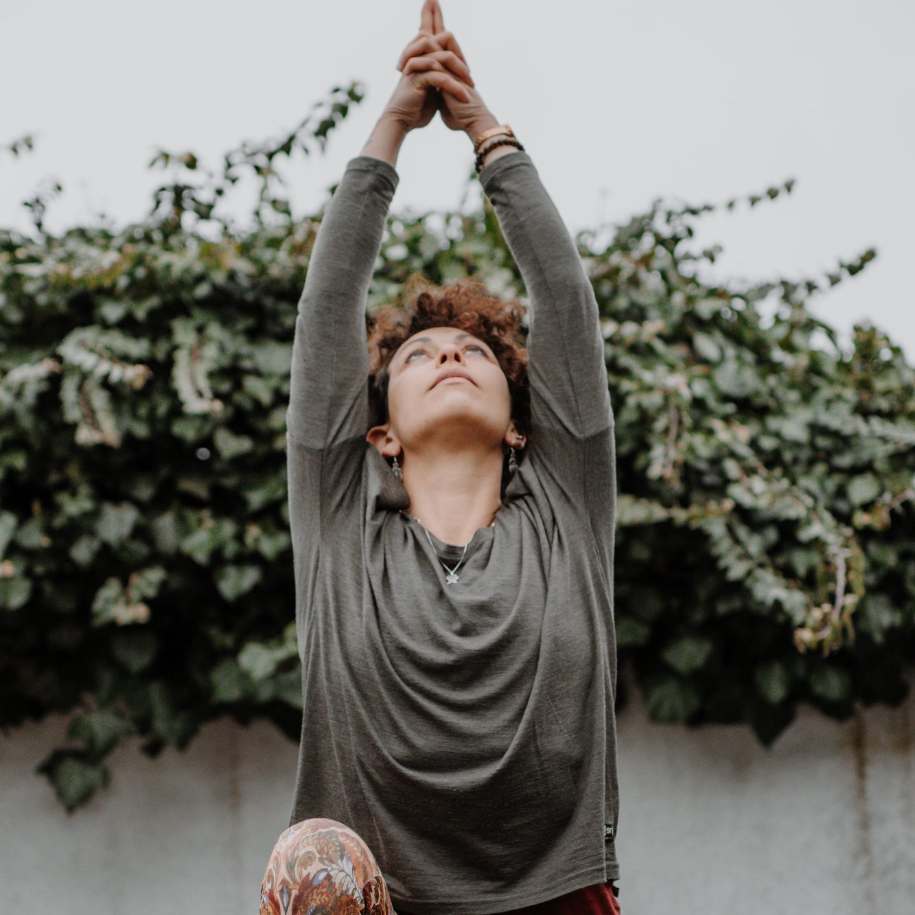 Eine Person in yoga-ähnlicher Pose vor einer bevölkerten Pflanzenwand.