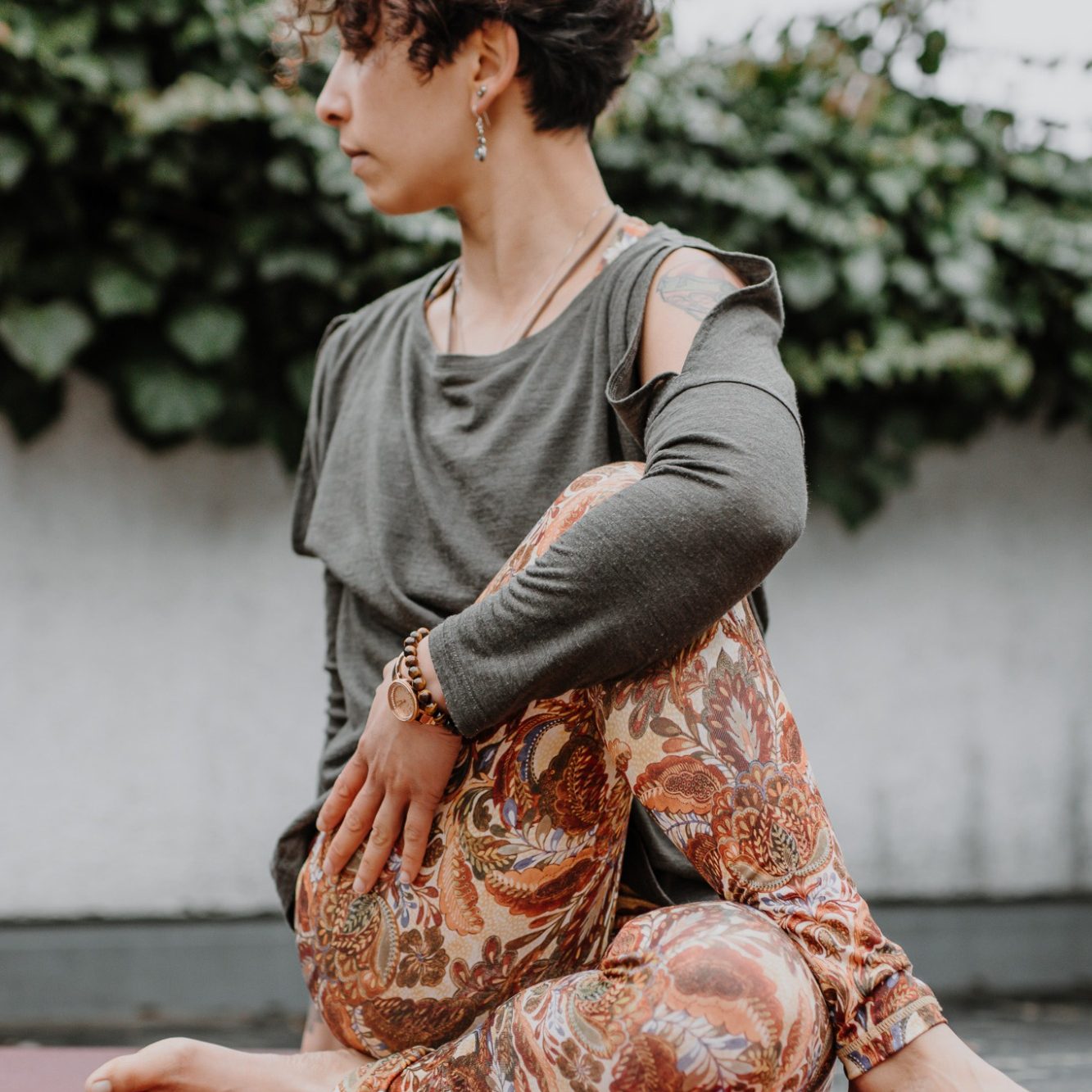 Eine Person in Yoga-Pose, trägt ein graues Oberteil und gemusterte Leggings.